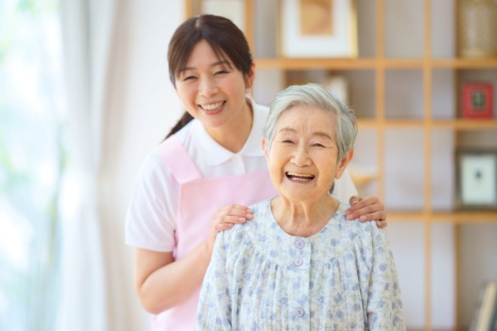 高齢者の肩に手を置き笑う女性介護士